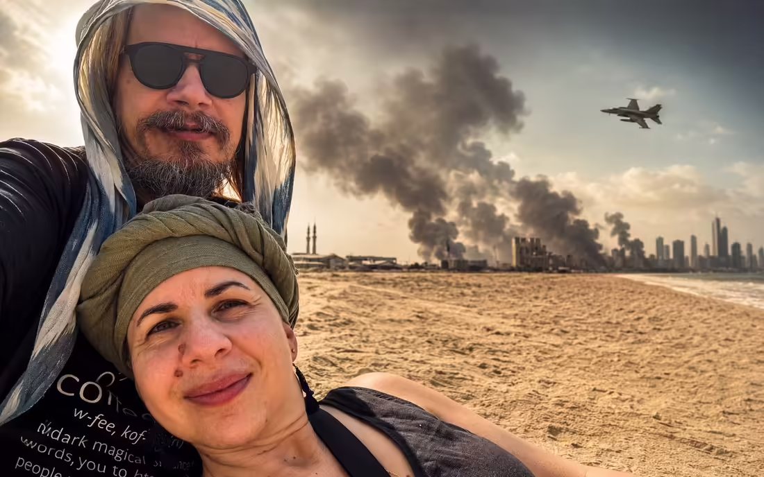 Dvojica cestovateľov na pláži v Sharjah, za nimi dym nad pobrežím smerom k Dubaju a vojenská stíhačka na oblohe.