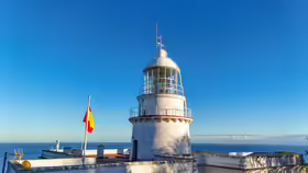 Biela veža majáka Faro de Punta Almina so španielskou vlajkou a Gibraltárskym prielivom v pozadí