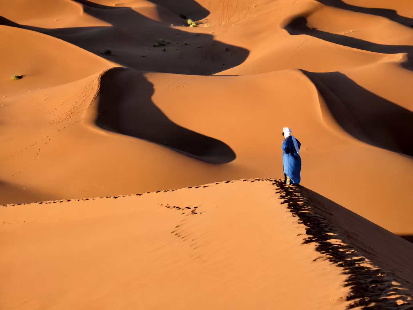 Osamelý pútnik v modrom odeve na pieskových dunách marockej Sahary