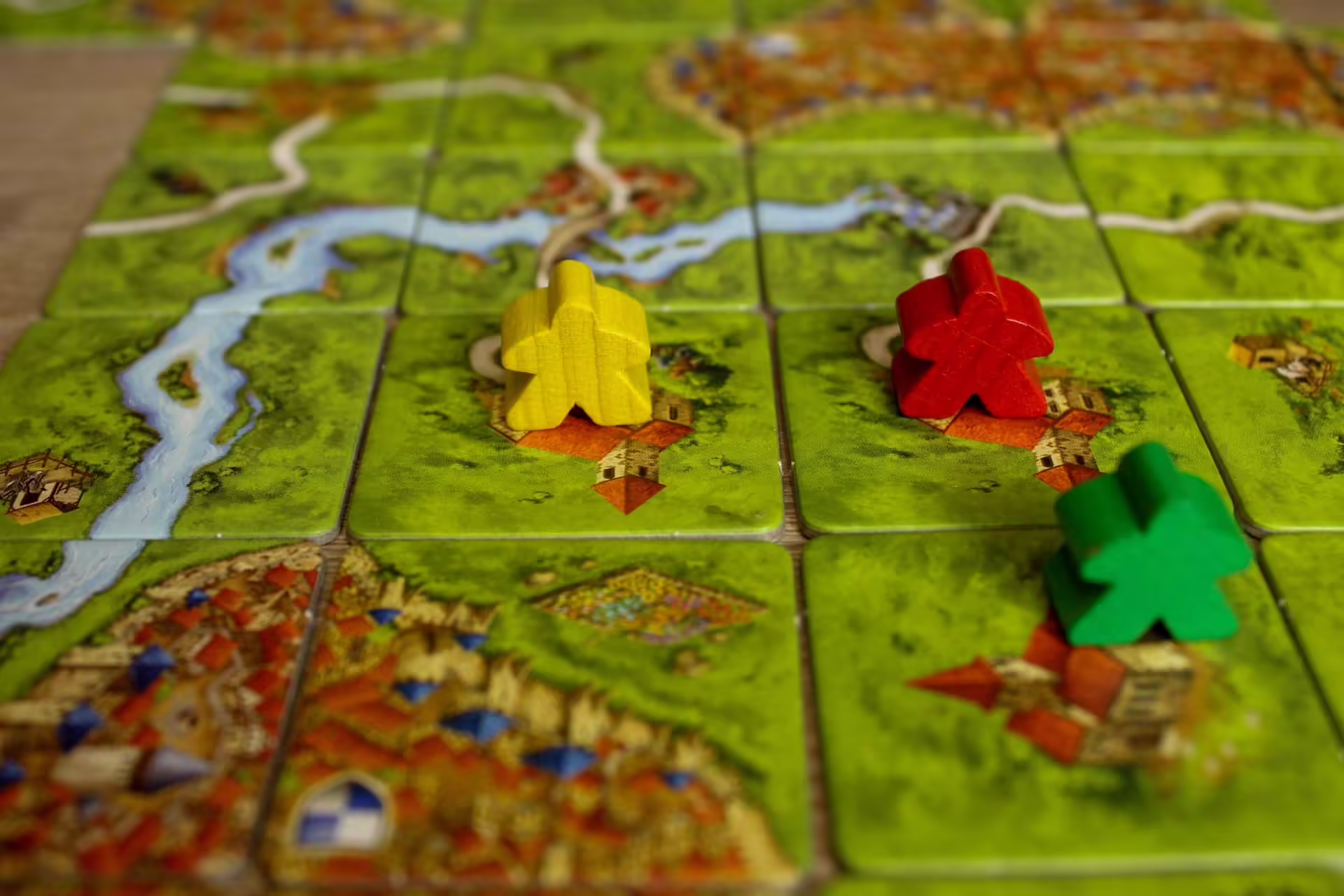 Rozohraná dosková hra Carcassonne s dielikmi krajiny a farebnými figúrkami meeple