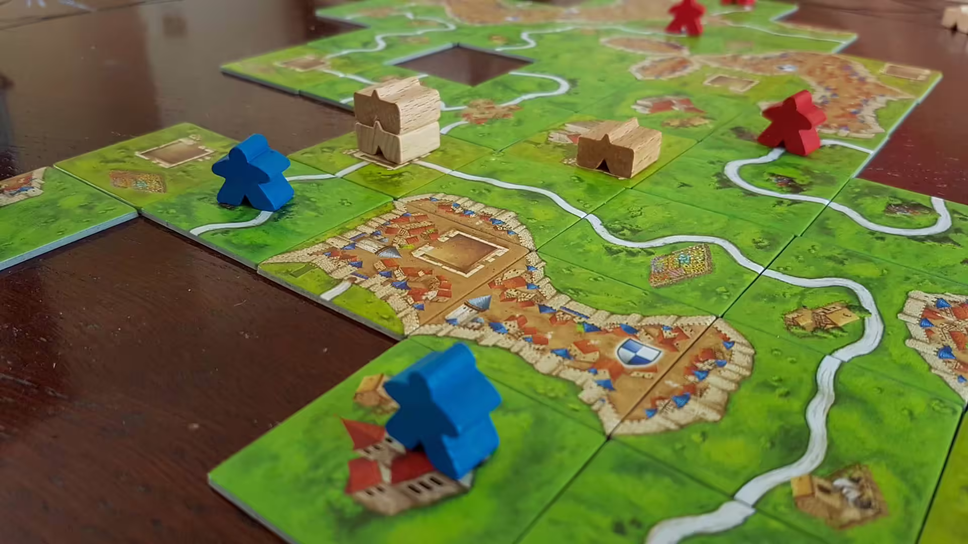 Rozložené dieliky doskovej hry Carcassonne s cestami, mestami a figúrkami