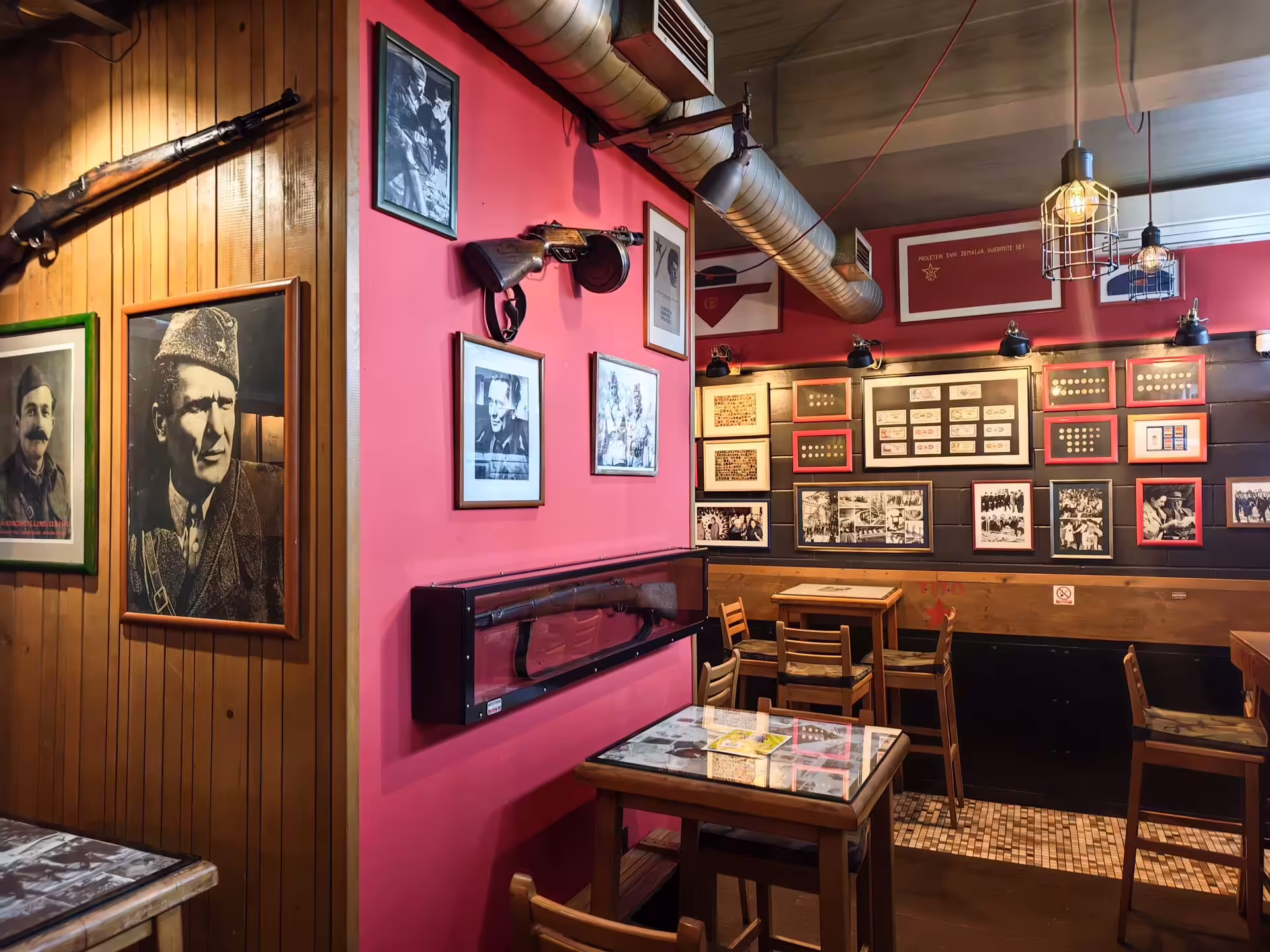 Interiér Cafe Tito v Sarajeve s historickými fotografiami, vojenskými exponátmi a červenou výzdobou