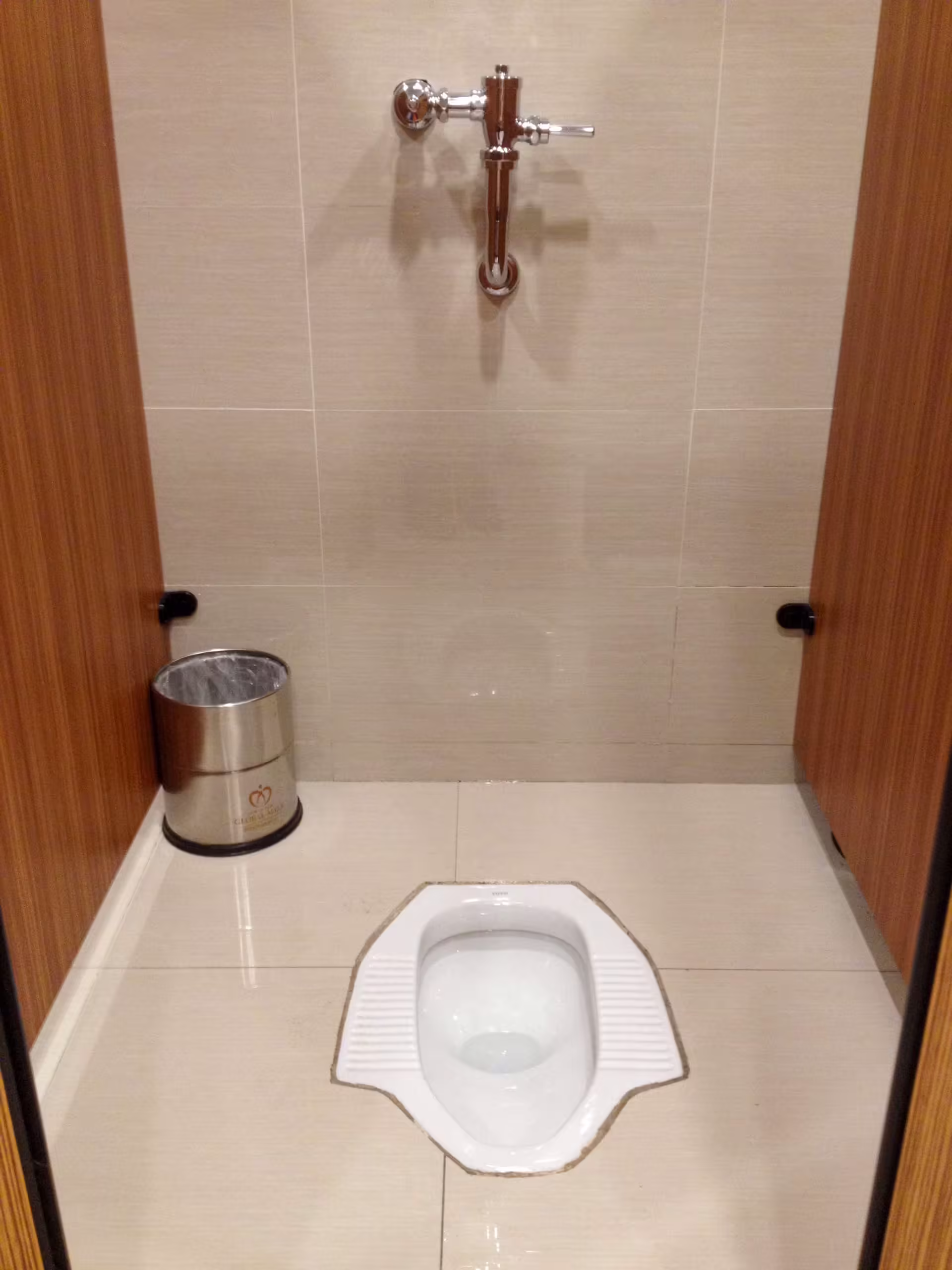 Squat toaleta v Číne zapustená do podlahy s nástenným splachovacím ventilom a košom