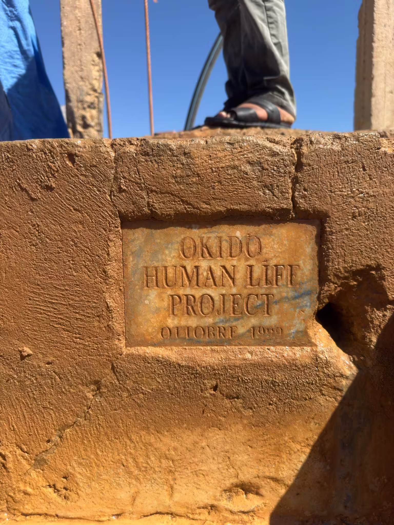 Kovová tabuľka OKIDO Human Life Project s dátumom október 1999 osadená v púštnej studni