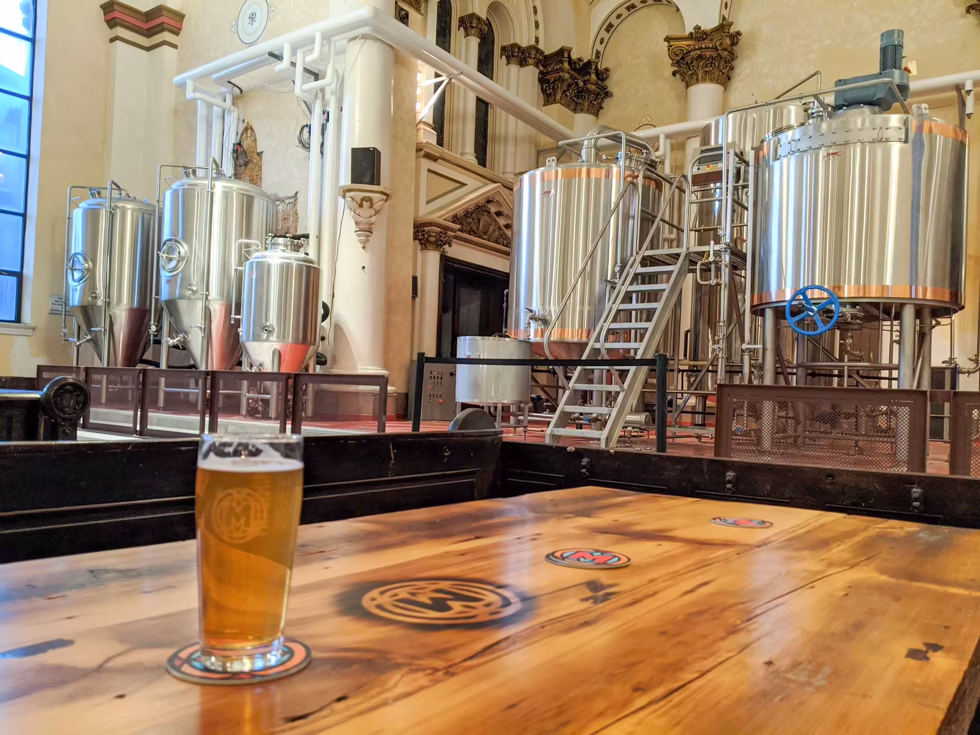 Pohár piva pred nerezovými varnými tankami Ministry of Brewing v bývalom kostole