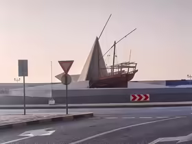 Drevená loď Al-Barraqah vystupujúca z bielej papierovej lode na kruhovom objazde pri Ajman Corniche