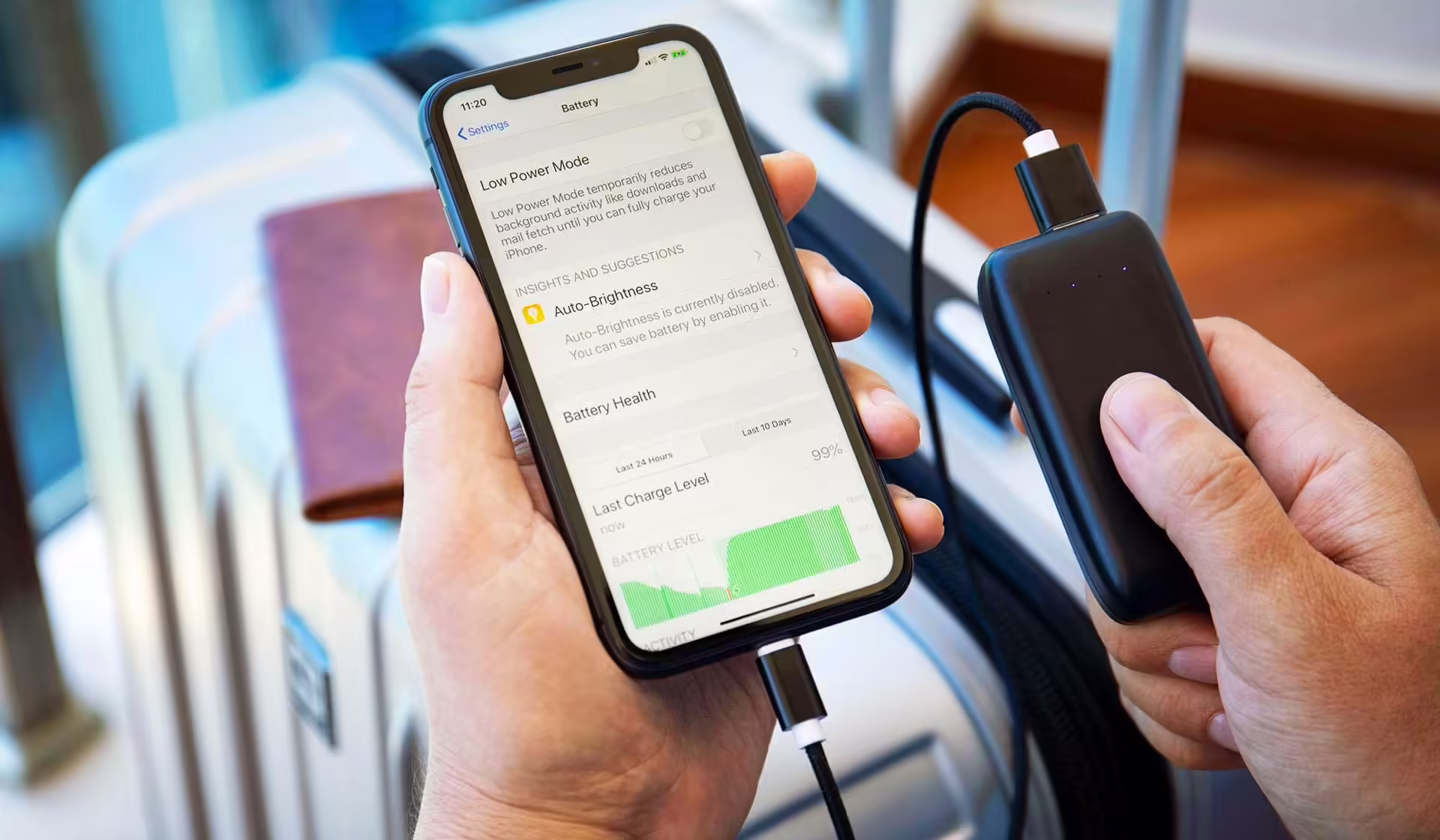 Ruky držiace iPhone s otvorenými nastaveniami batérie a čiernu powerbanku pripojenú káblom