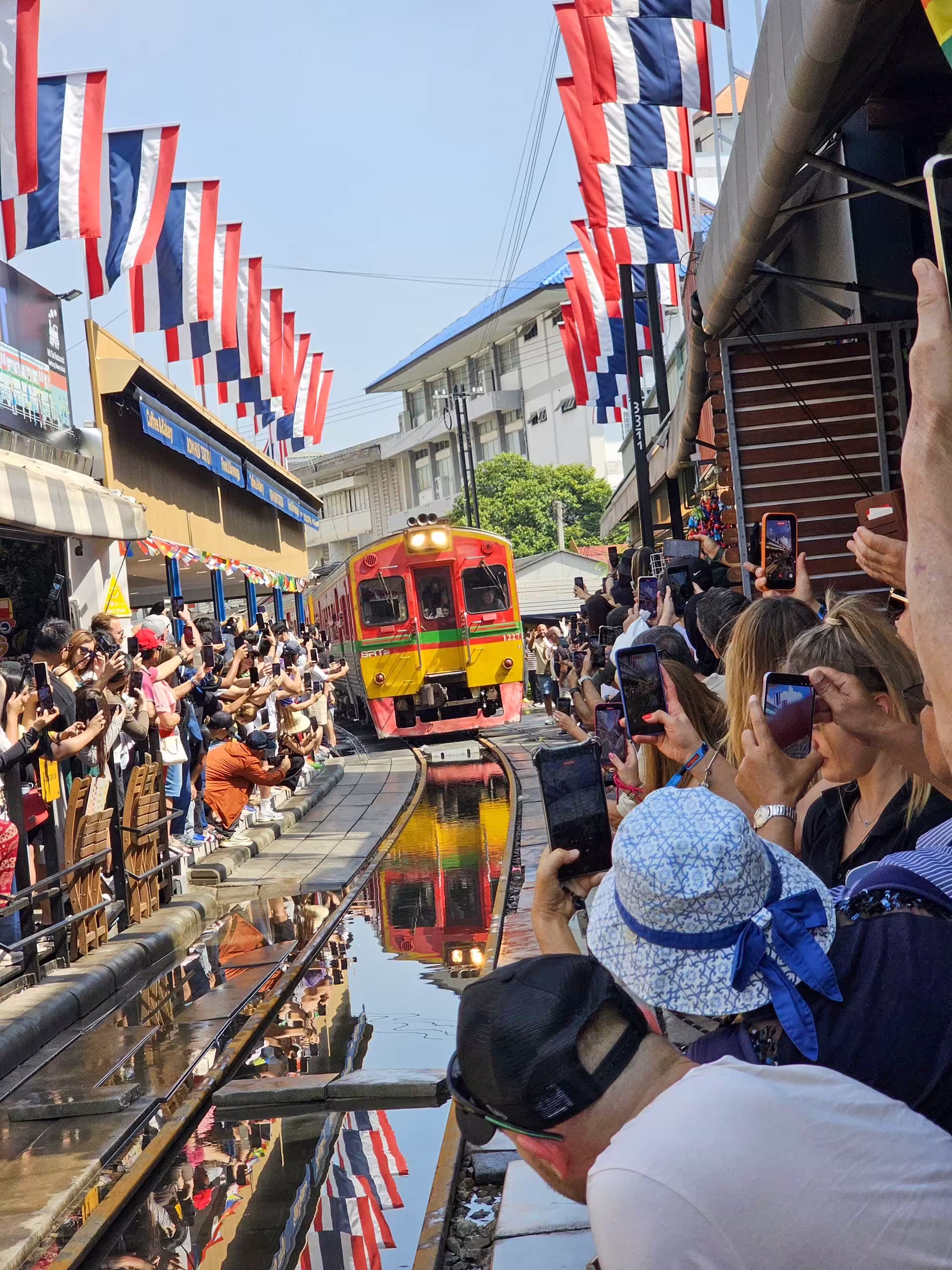 Dav turistov fotografuje prichádzajúci vlak na trhu Maeklong Railway Market